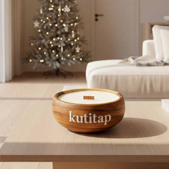 Candle in a wooden holder with 'kutitap' branding on a textured surface with green foliage in the background